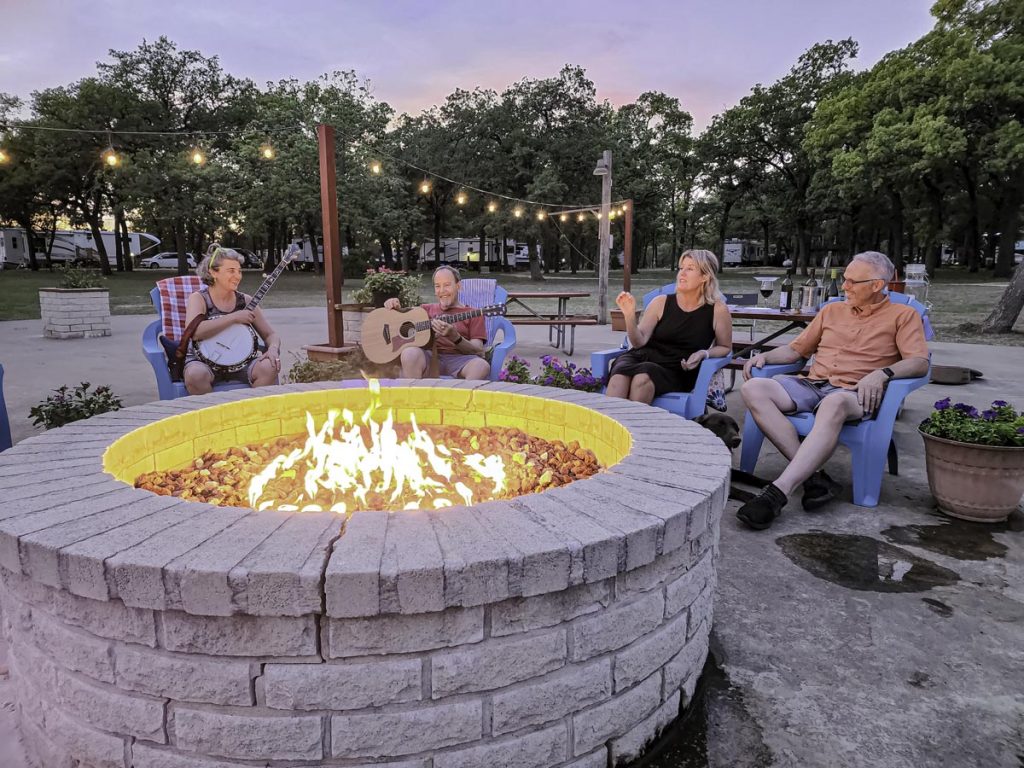 people laughing and talking around a fire pit at dusk