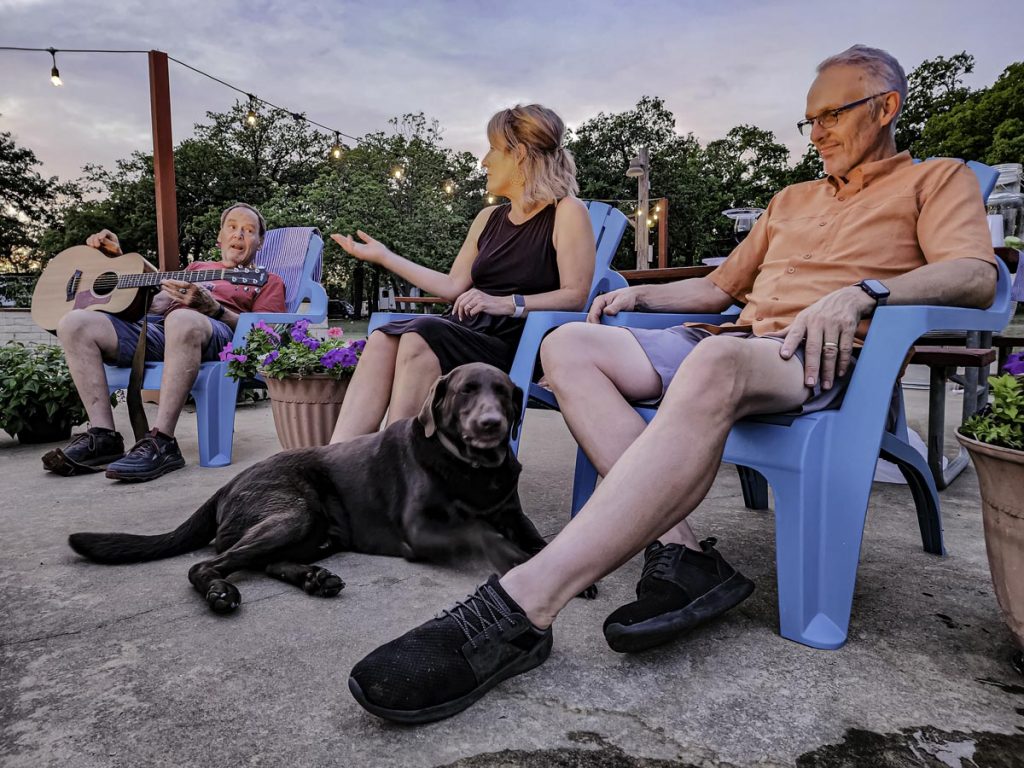 people laughing around a fire pit at dusk with a dog
