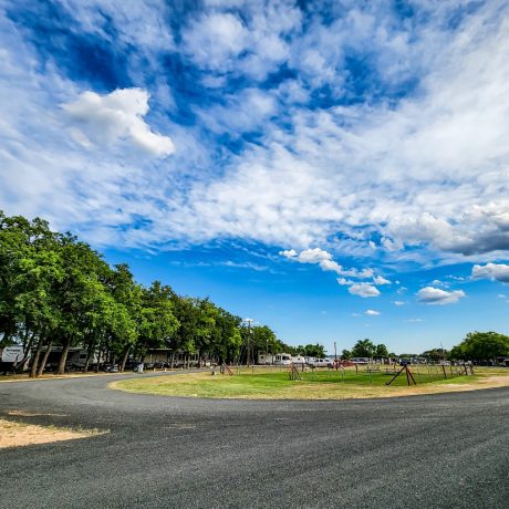 A tranquil view of the entrance under mature oak trees, showcasing the serene and well-maintained environment at Oakwood RV Resort in Fredericksburg, TX.