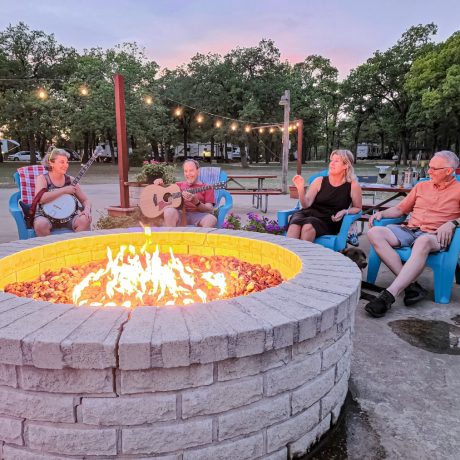 A happy friends singing and playing instruments at Oakwood RV Resort in Fredericksburg, TX, surrounded by beautiful shady views and rustic charm.