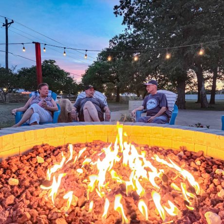 A happy friends singing and playing instruments at Oakwood RV Resort in Fredericksburg, TX, surrounded by beautiful shady views and rustic charm.