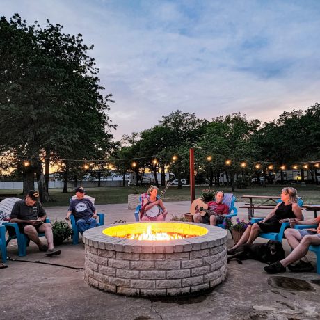 A happy friends singing and playing instruments at Oakwood RV Resort in Fredericksburg, TX, surrounded by beautiful shady views and rustic charm.