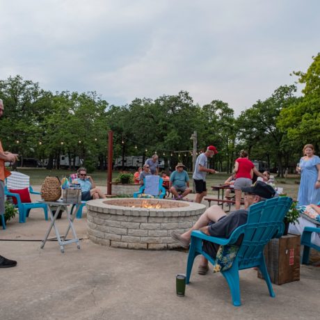 A happy friends singing and playing instruments at Oakwood RV Resort in Fredericksburg, TX, surrounded by beautiful shady views and rustic charm.